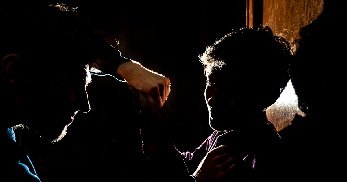 Two Men, Backlit By Lamplight, Fighting In The Dark, With One Man Raising His Fist To Strike The Other