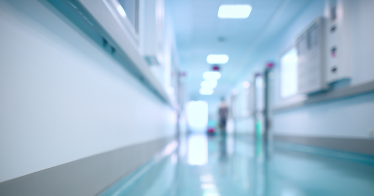 A Slightly Out Of Focus View Down A Green-Floored Hospital Hallway, With A Figure Walking In The Distance