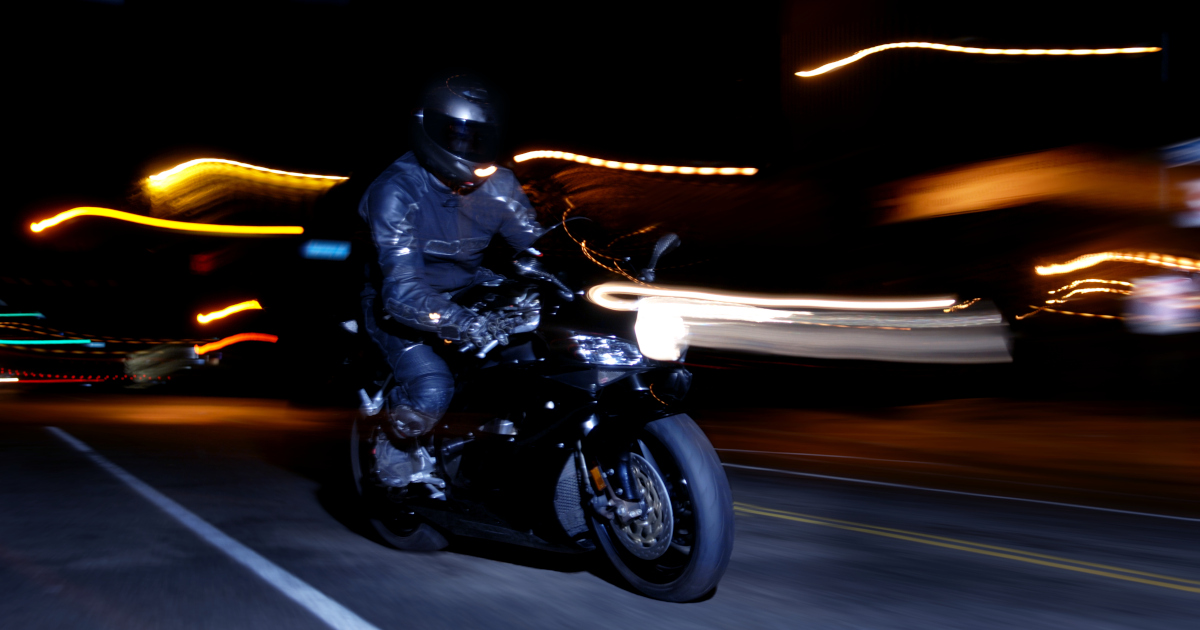 A Helmeted Figure On A Motorcyle Streaking Down A City Street At Night