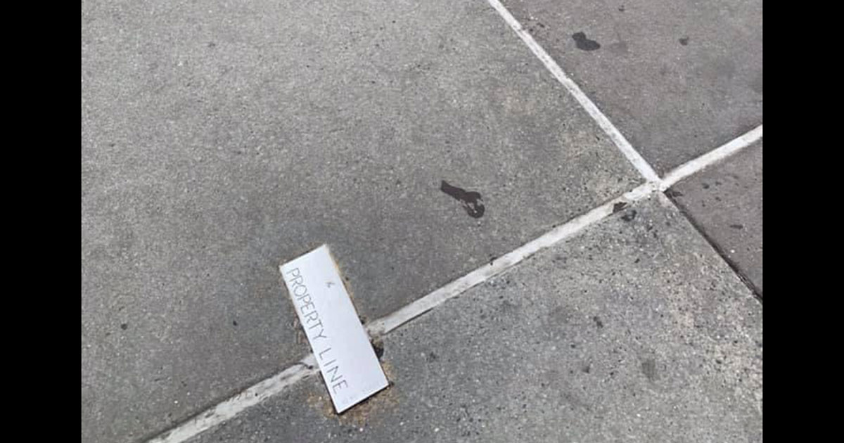 A small metal plaque marks a property line on a New York City sidewalk