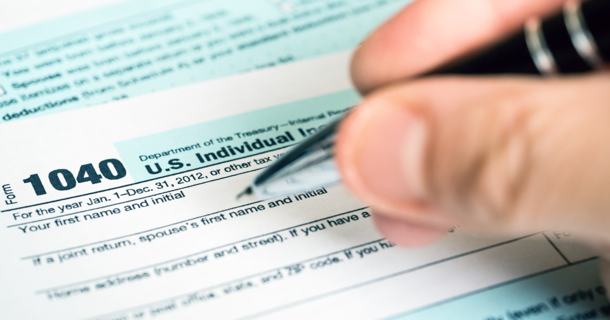 A Person Holds A Ballpoint Pen Poised Above The Name Section Of A Form 1040 