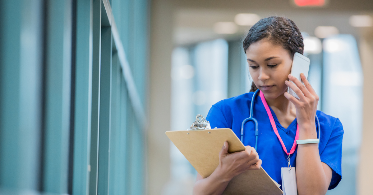 Nurse In Blue Scrubs Talking On Her Cell Phone While Looking At Patient’s Chart