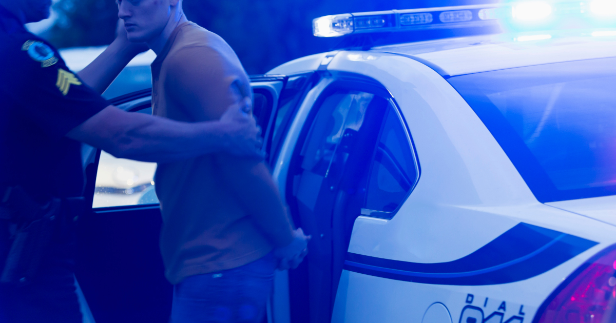 A Policeman Helping A Handcuffed Man Into The Back Seat Of A Squad Car