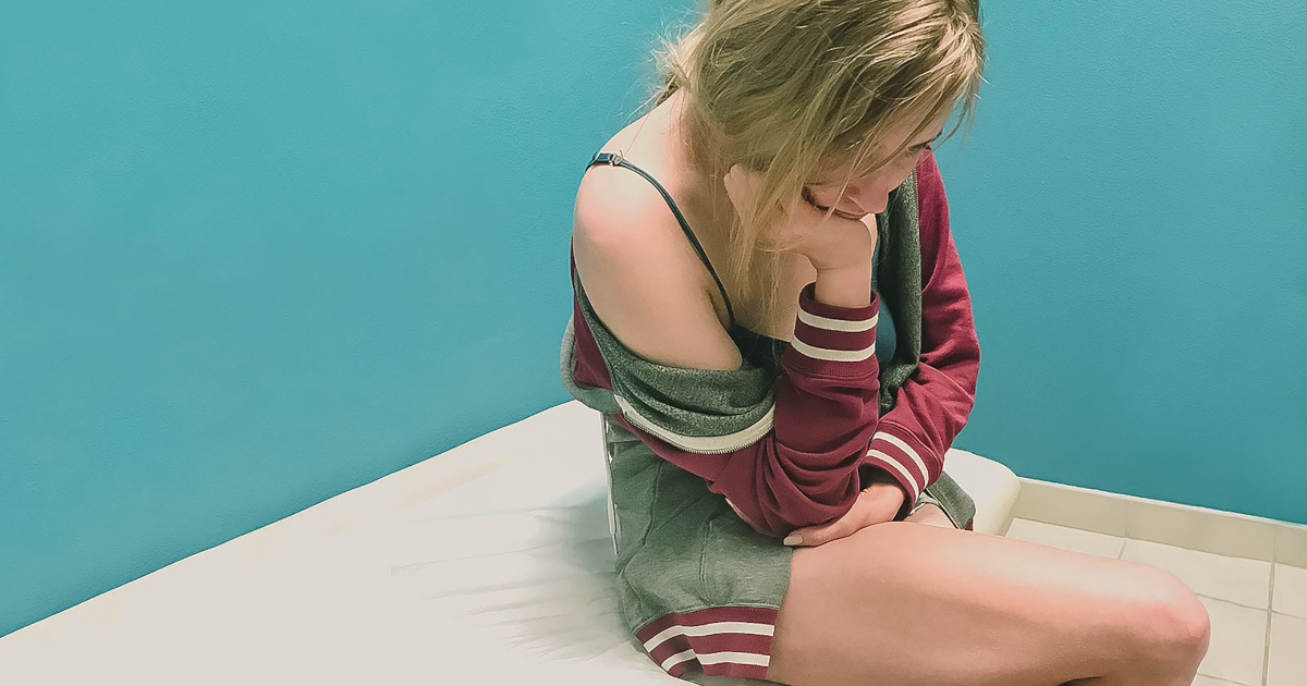 Young Woman In Underclothes Sitting On A Medical Exam Table, Looking Down At The Floor