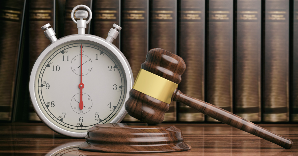 A Stopwatch Sits Atop A Conference Table Next To A Judge’s Gavel With Law Books In The Background