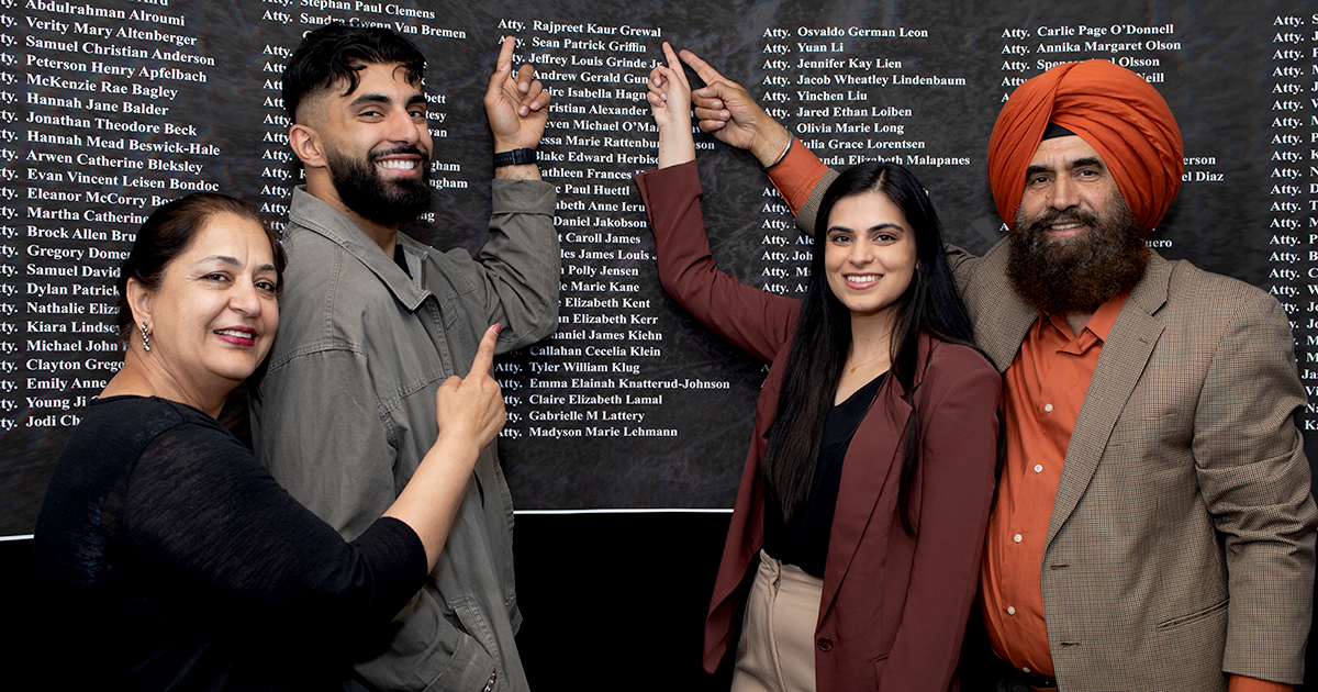 four smiling people stand before a poster with a list of names