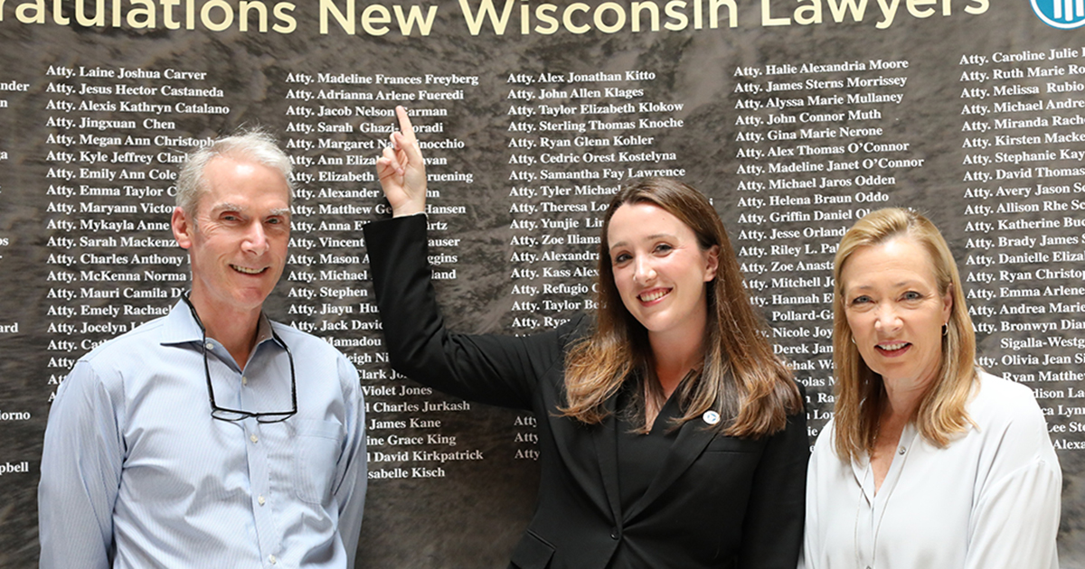 Three people stand in front of the list of names of 170 new lawyers