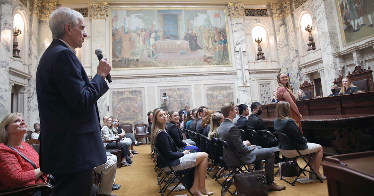 A man stands and speaks in a microphone in the Supreme Court Hearing Room