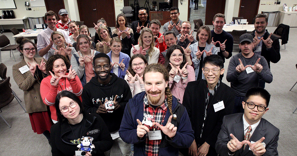 A group of about 30 people smiling at the camera and showing the UW 'W' with their hands