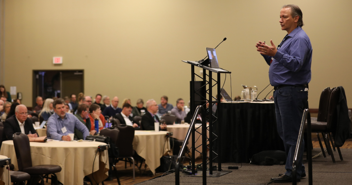 A man on a stage talks to a crowded audience