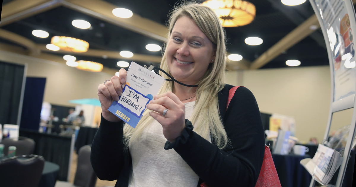 a woman smiles at the camera and holds up her name badge