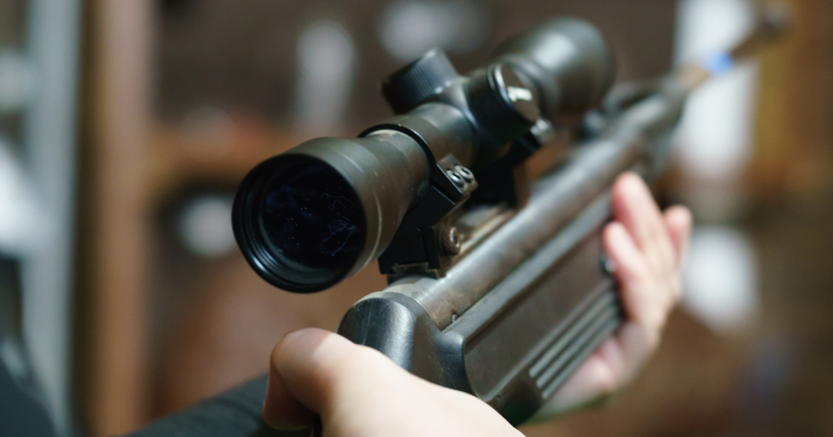 A Woman’s Hands Cradling A Rifle Outfitted With A Scope