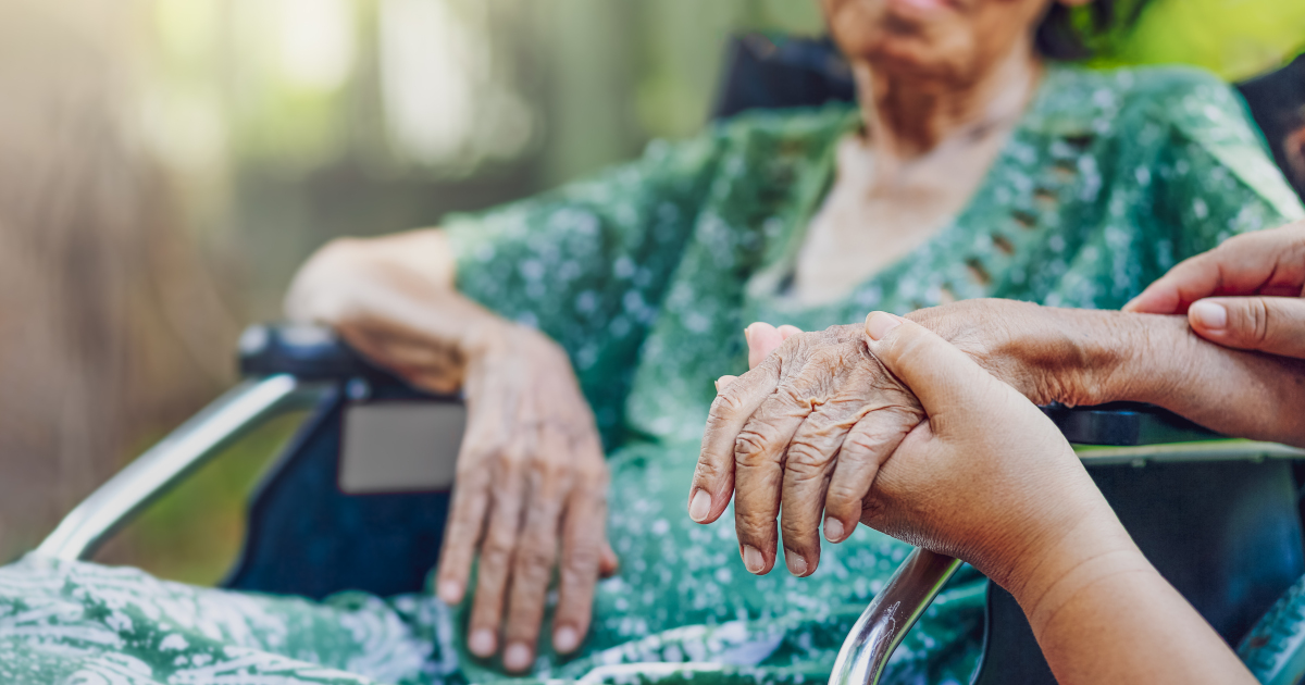 Old Woman In Wheelchair With Nurse Holding Her Hand