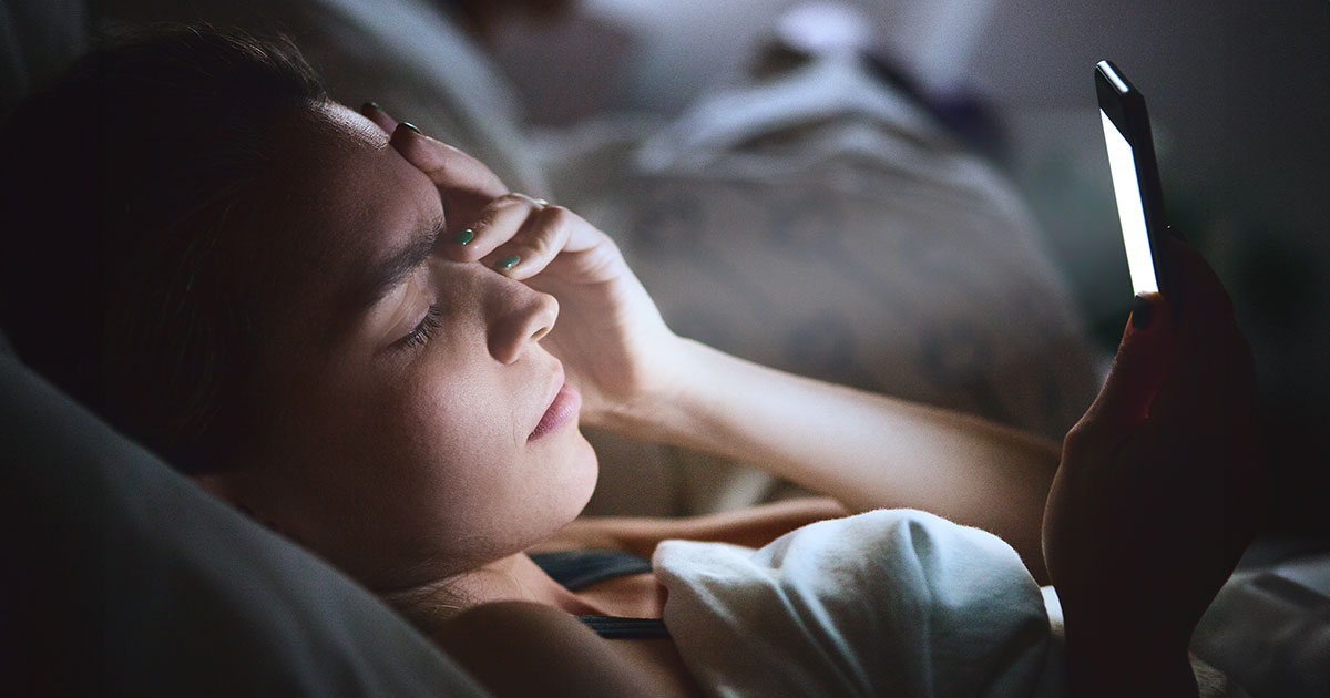 stressed person looking at phone in bed