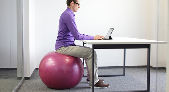 man sitting on medicine ball at desk