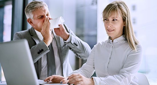 businessman sneezes in coworkers face